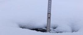 Miara wbita w w pokrywę śniegu na dachu budynku.