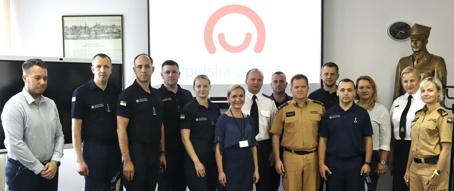 Zdjęcie uczestników projektu na tle loga Polska Pomoc, po bokach krzesła