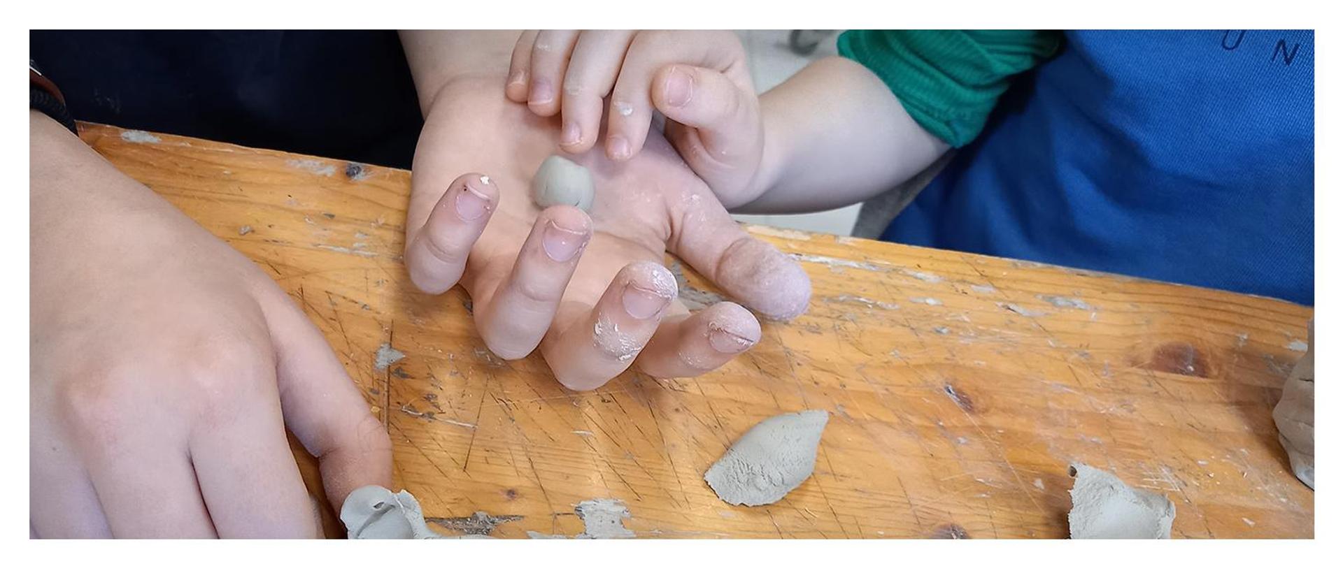 duża dłoń trzymająca kawałek plasteliny i mała dłoń oparta o nią