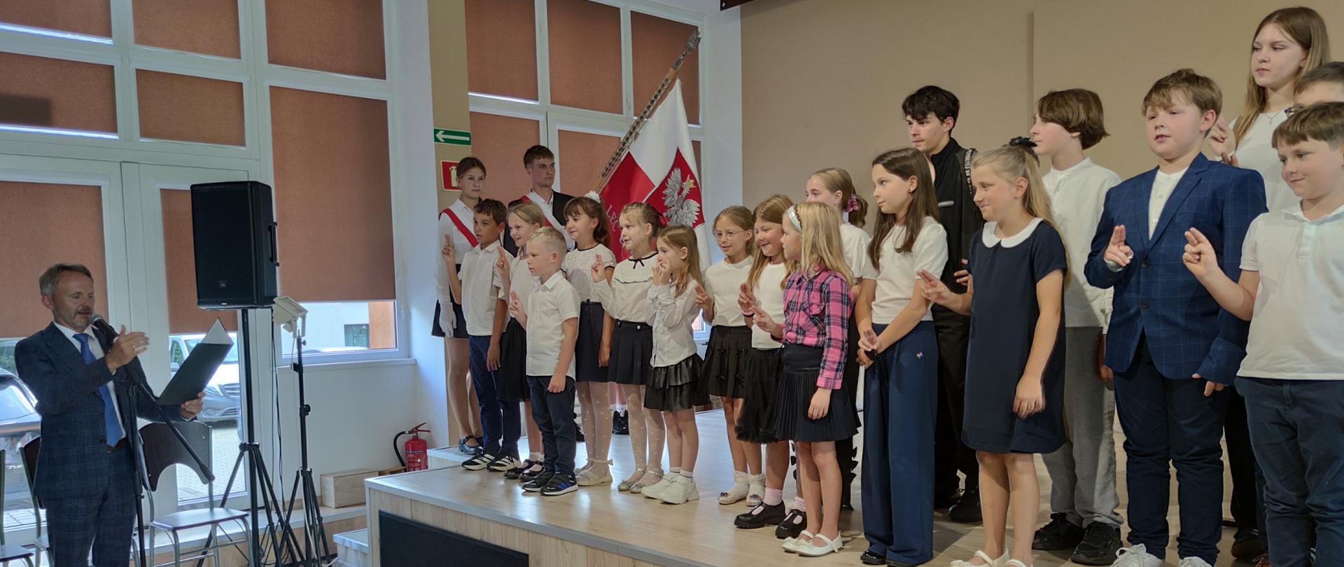 przemawiający dyrektor i uczniowie stojący na scenie