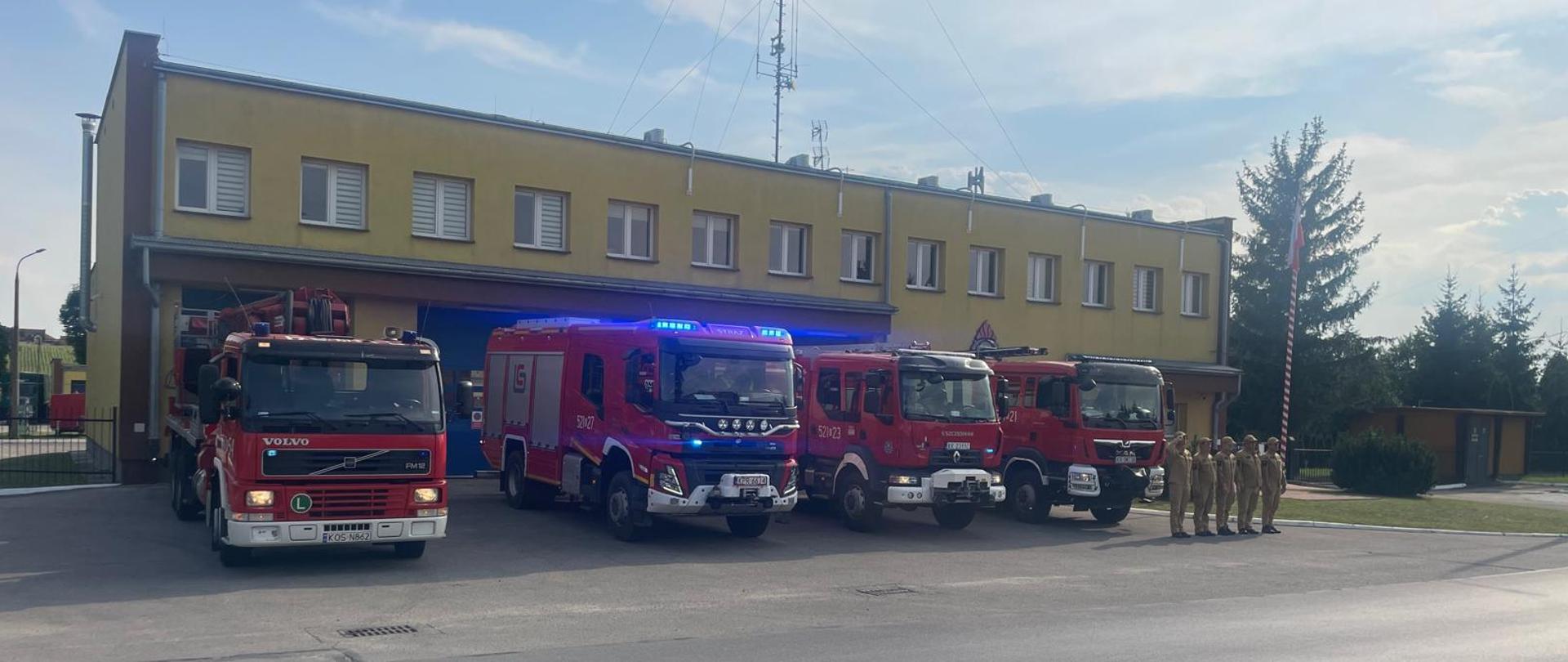 Hołd Bohaterom Powstania Warszawskiego - strażacy oddają honory na tle samochodów ratowniczych przed garażem 