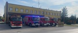 Hołd Bohaterom Powstania Warszawskiego - strażacy oddają honory na tle samochodów ratowniczych przed garażem 