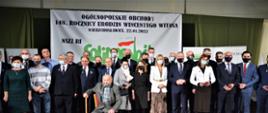 Uczestnicy zgromadzeni do wspólnego zdjęcia przed plakatem zatytułowanym: Ogólnopolskie obchody 148. rocznicy urodzin Wincentego Witosa, Wierzchosławice, 22.01.2022
