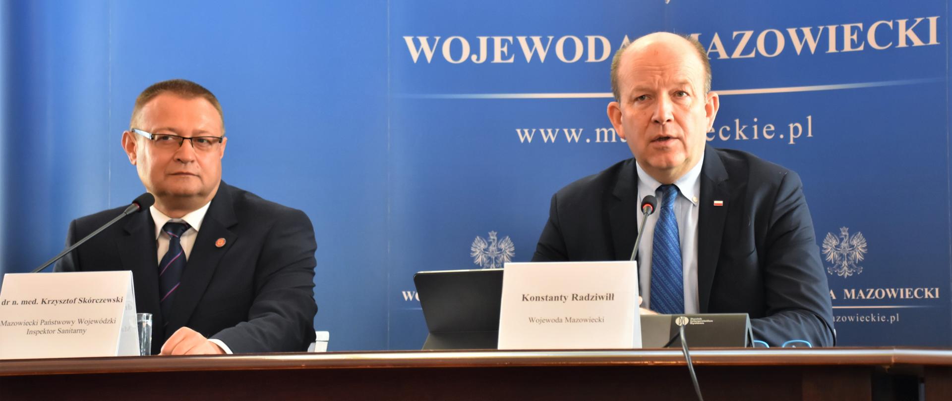 Przy stole prezydialnym siedzą Wojewoda Mazowiecki Konstanty Radziwiłł oraz Mazowiecki Państwowy Wojewódzki Inspektor Sanitarny dr. n. med. Krzysztof Skórczewski. W tle niebieska ścianka z napisem Wojewoda Mazowiecki. 