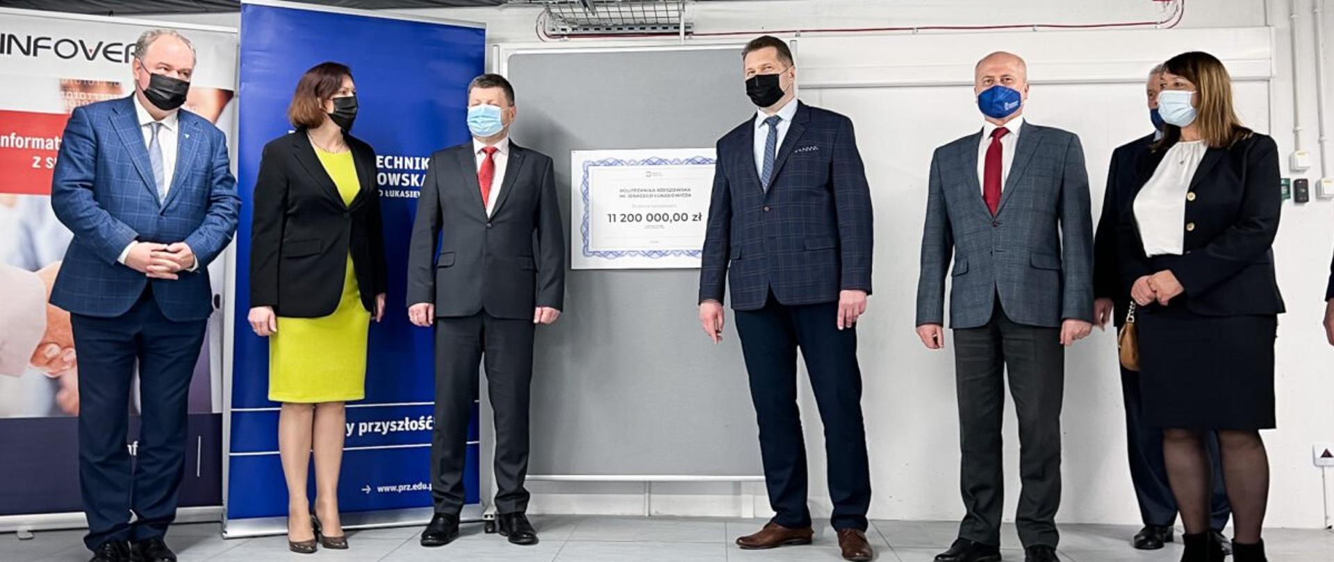 Minister Edukacji i nauki Przemysław Czarnek wraz z wojewodą podkarpackim Ewą Leniart, wicemarszałkiem województwa podkarpackiego Piotrem Pilchem, posełm na Sejm RP Teresą Pamułą oraz z przedstawicielami Politechniki Rzeszowskiej pozuje do zdjęcia obok wiszącego na ścianie symbolicznego czeku z napisem 11 200 00,00