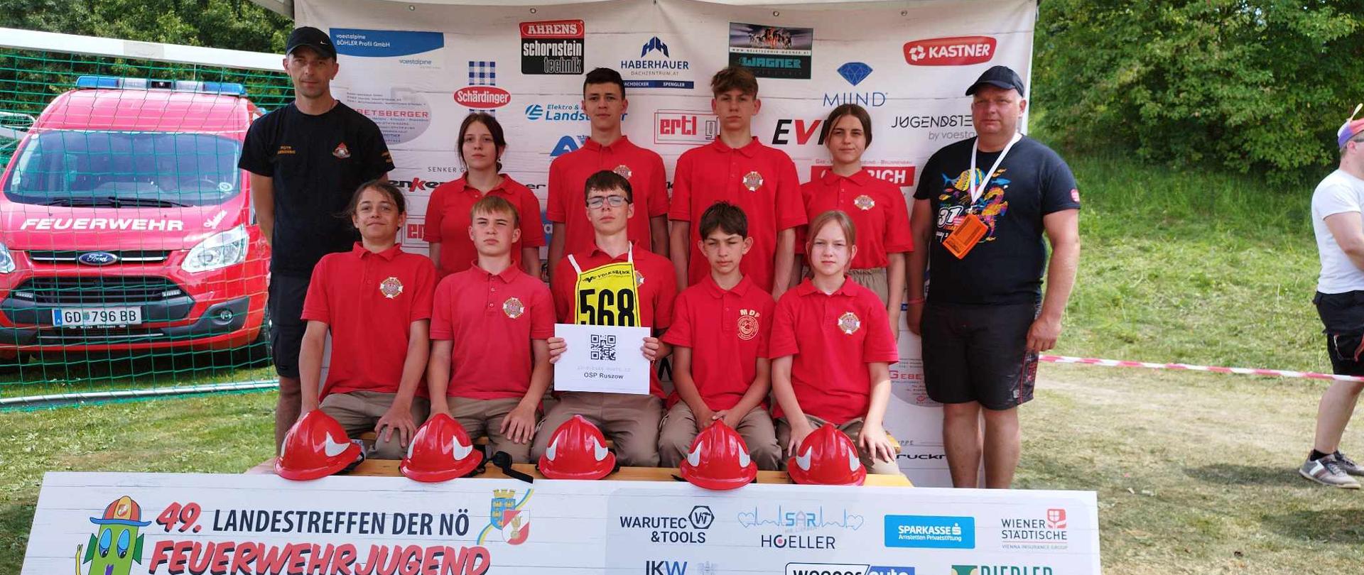 Młodzież wraz z opiekunami stojąca na tle banera.