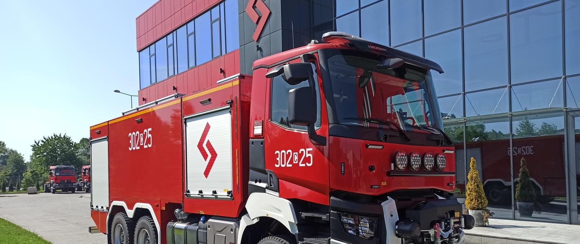 Na zdjęciu samochód ratowniczo-gaśniczy. Widok z przodu, prawy skos. Prezentacja auta. W tle obiekt fabryki.