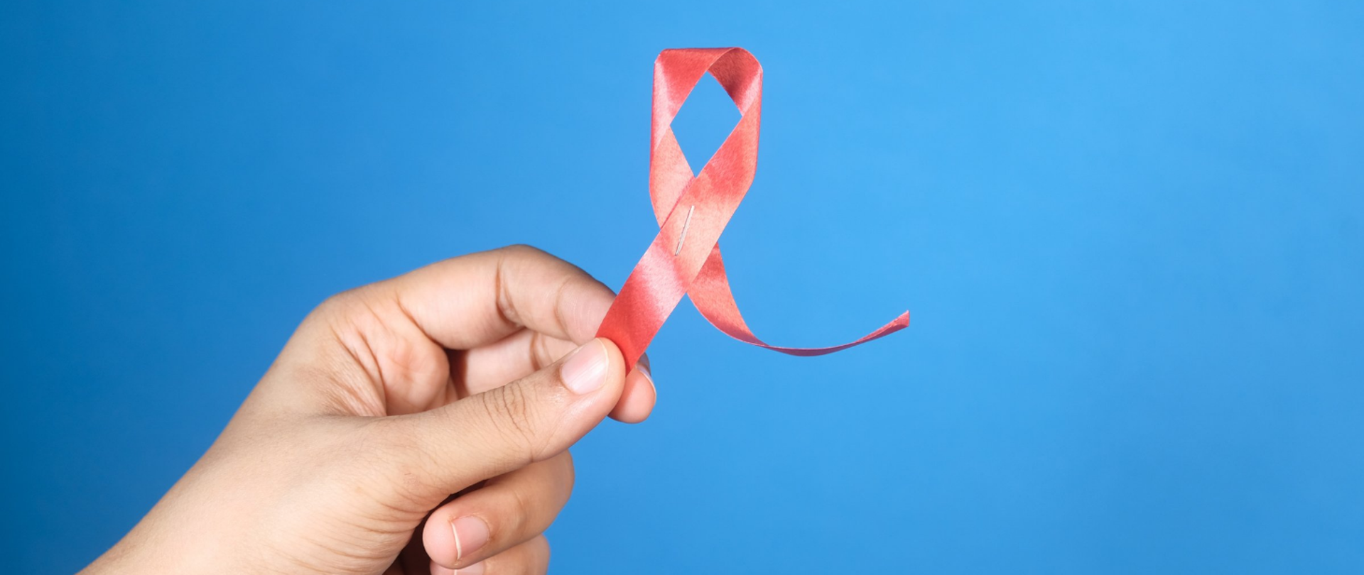 Na niebieskim tle z lewej strony dłoń trzymająca czerwoną wstążeczkę