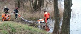 Trzej strażacy sprawiający wkładający do wody jeziora pompę pływającą