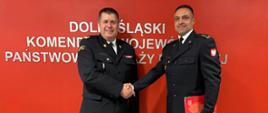 Strażacy w ciemnych mundurach na tle jaskrawoczerwonej ściany z białym napisem "Dolnośląski Komendant Wojewódzki Państwowej Straży Pożarnej"