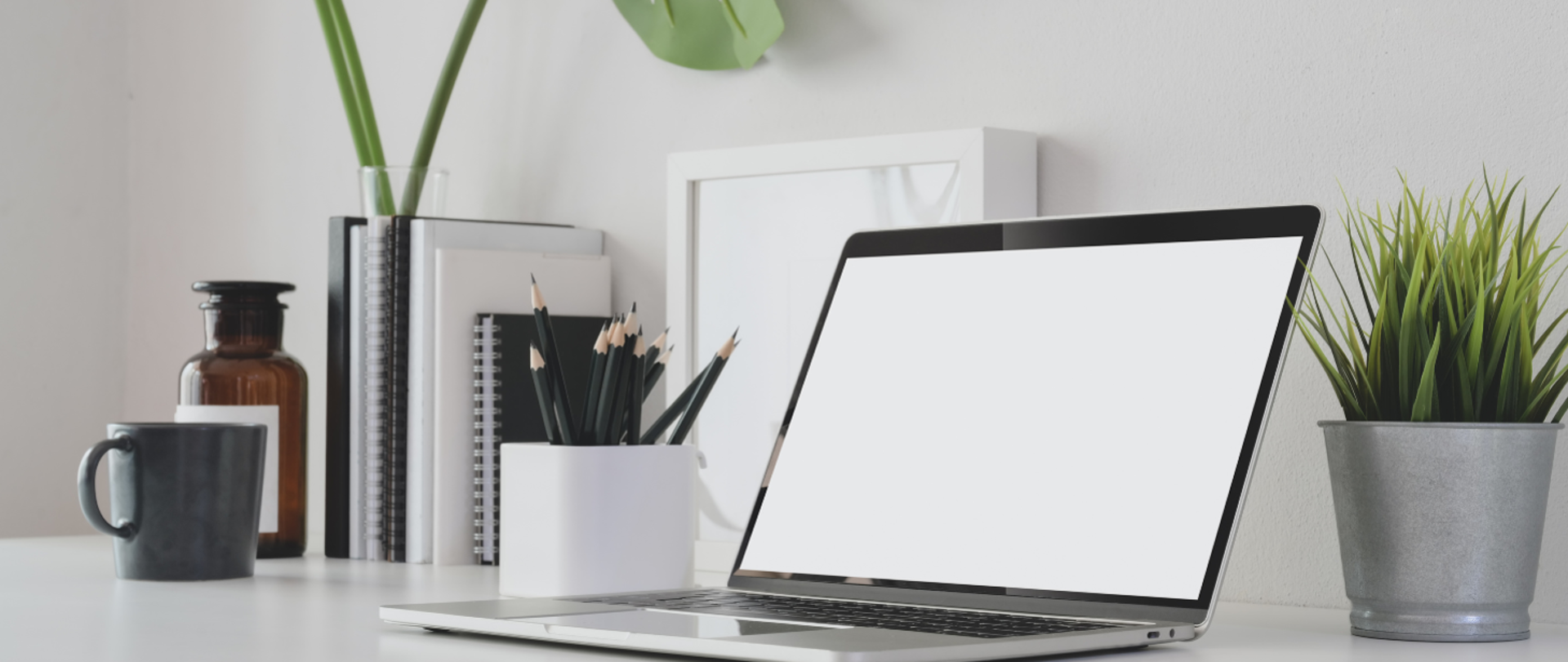 Blat biurka na którym znajduje się na pierwszym planie laptop a w oddali ołówki i notes