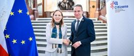 Minister funduszy i polityki regionalnej Katarzyna Pełczyńska-Nałęcz i wicepremier oraz minister rozwoju regionalnego Czech Ivan Bartoš ściskają sobie dłonie, za nimi schody, a obok flagi Polski i UE 