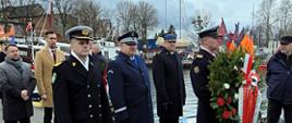 Funkcjonariusze Ministerstwa Spraw Wewnętrznych i Administracji stoją za żołnierzem Marynarki Wojennej RP, który trzyma wieniec. 