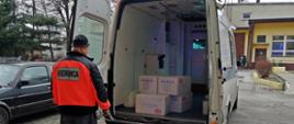 Kierowca z ZZOZ Wadowice stoi za samochodem dostawczym, w którym ułożone są paczki z maseczkami ochronnymi.