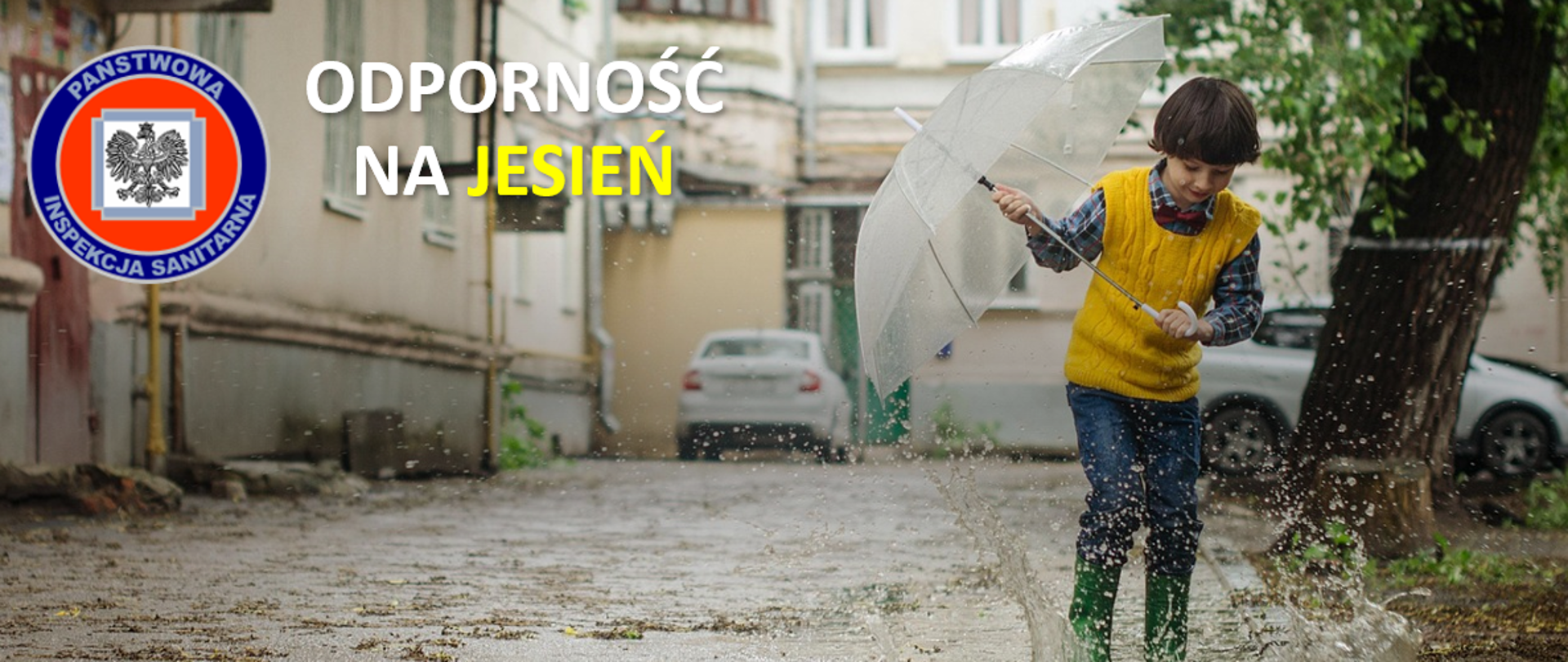 grafika przedstawia chłopca z parasolem i w gumowcach, które umożliwiają mu zabawę w kałuży