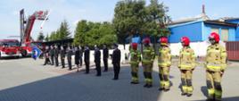 Zdjęcie wykonano podczas uroczystości Obchodów Dnia Strażaka w Komendzie Powiatowej Państwowej Straży Pożarnej w Sępólnie Krajeńskim. Na zdjęciu widzimy pododdziały Komendy Powiatowej Państwowej Straży Pożarnej w Sępólnie Krajeńskim podczas podnoszenia Flagi Państwowej. Od prawej zastęp pięciu strażaków w ubraniach specjalnych dalej strażacy ubrani w mundury galowe i służbowe ustawieni w dwuszeregu. W tle samochód gaśniczy oraz podnośnik, na którym powiewa biało czerwona flaga. Wszyscy uczestnicy ceremonii mają na sobie maseczki jednorazowe. 