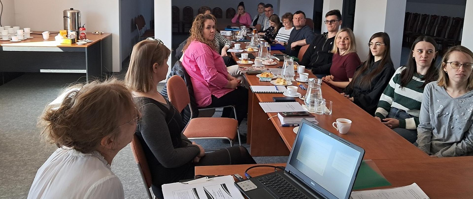 Zdjęcie poziome przestawiające próbobiorców urzędowych z Oddziałów Wojewódzkiego Inspektoratu Ochrony Roślin i Nasiennictwa w Kielcach oraz próbobiorców akredytowanych z firmy KLC Seeds Sp. z o.o. uczestniczących w szkoleniu dotyczącym pobierania prób materiału siewnego. Pracownik Działu Nadzoru Nasiennego w Kielcach w pozycji siedzącej omawia prezentację multimedialną.
