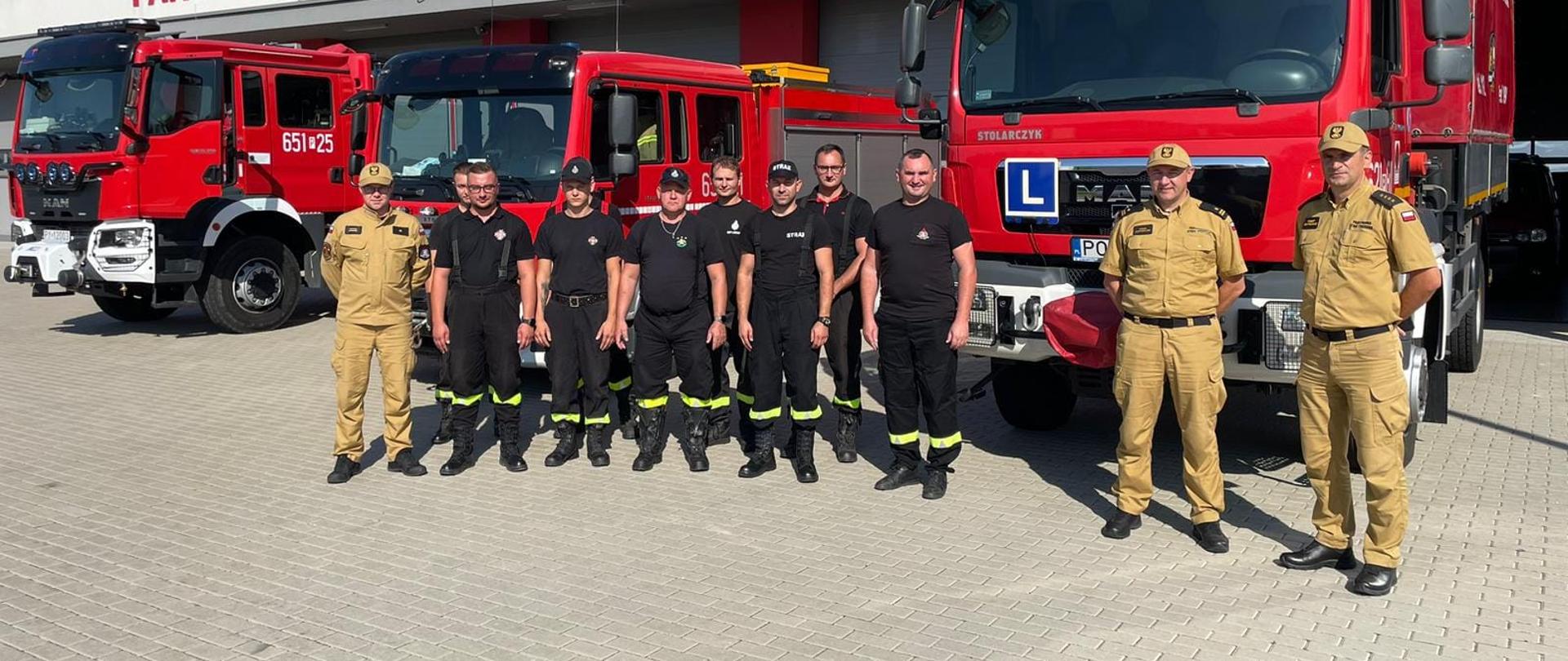 Zdjęcie przedstawia jedenastu strażaków stojących przed trzema wozami strażackimi. z tyłu napis Państwowa Straż Pożarna
