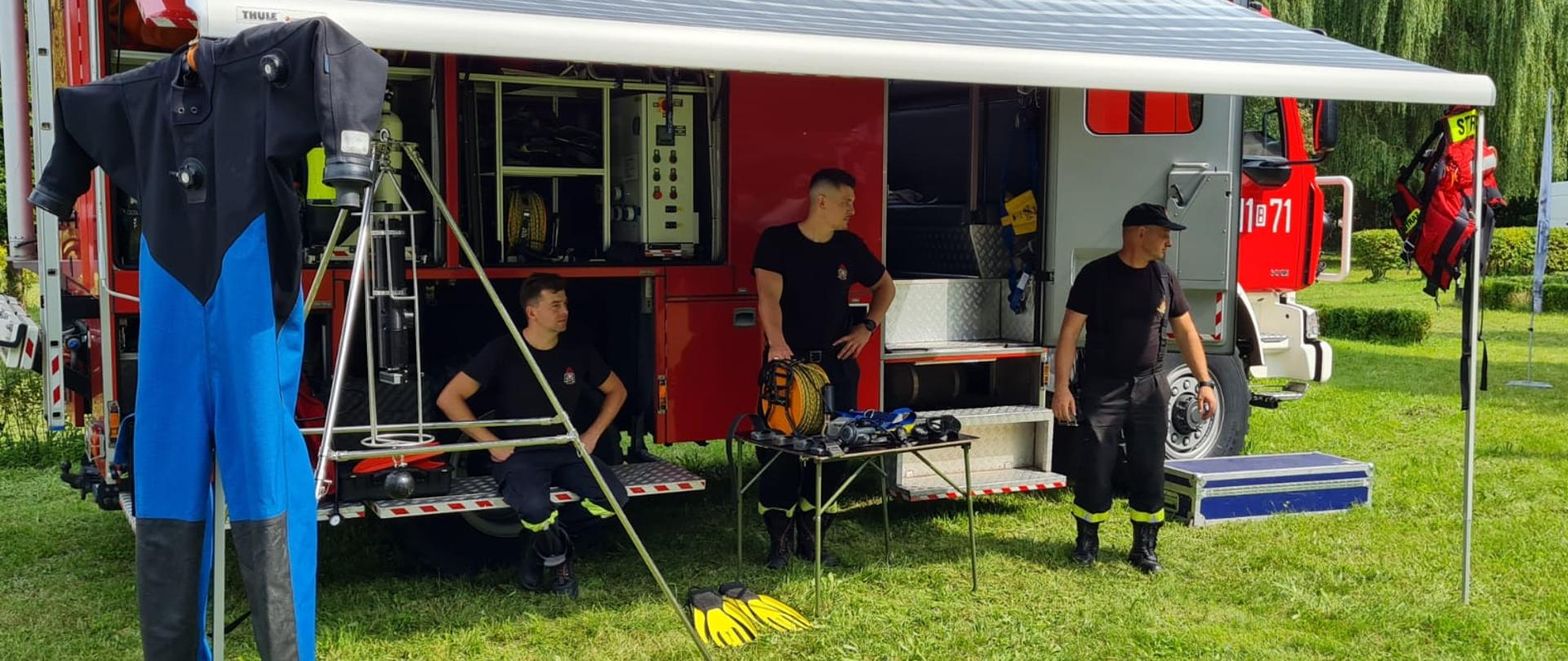 Strażacy przy samochodzie ratownictwa wodnego i rozstawionym sprzętem.