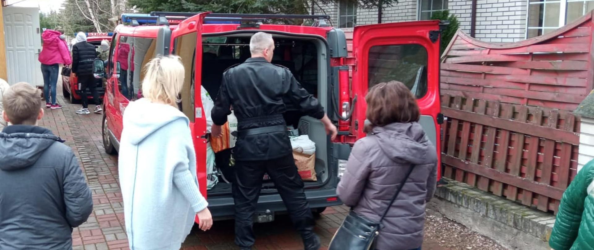 Zdjęcie przedstawia strażaków Komendy Powiatowej Państwowej Straży Pożarnej w Gołdapi, którzy we współpracy z przedstawicielami Starostwa Powiatowego w Gołdapi, udzielają pomocy w transporcie uchodźcom z Ukrainy (w tym pakowanie bagażów) przy użyciu pojazdów pożarniczych