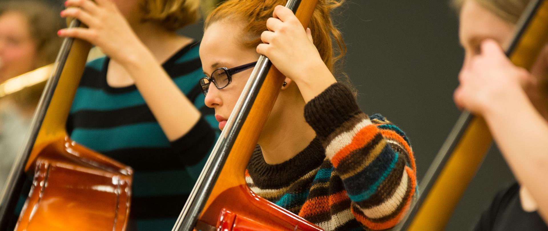 Grafika przedstawia osoby grające na kontrabasach