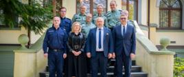 Grupa osób stoi na schodach przed wejściem do żółtego budynku.