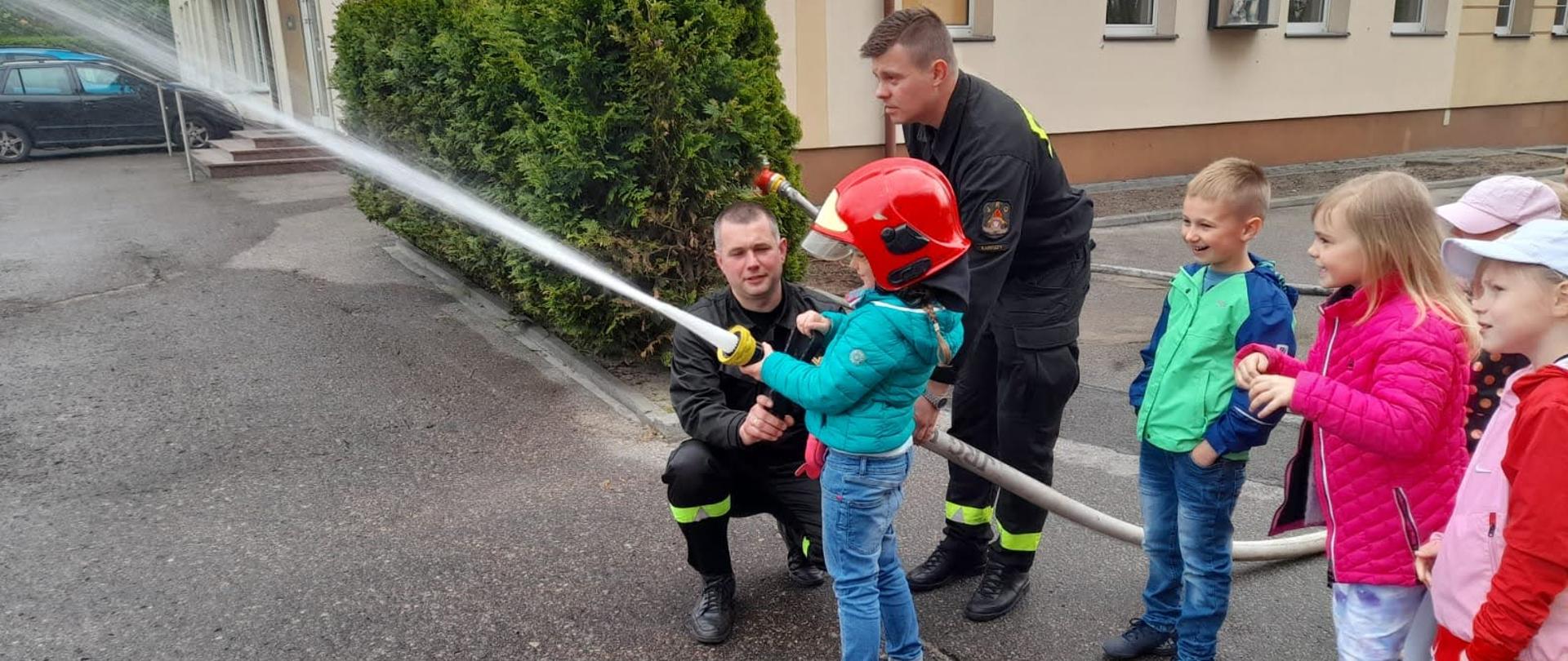 Dzieci obsługujące prądownicę wodną pod nadzorem strażaków