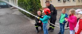 Dzieci obsługujące prądownicę wodną pod nadzorem strażaków