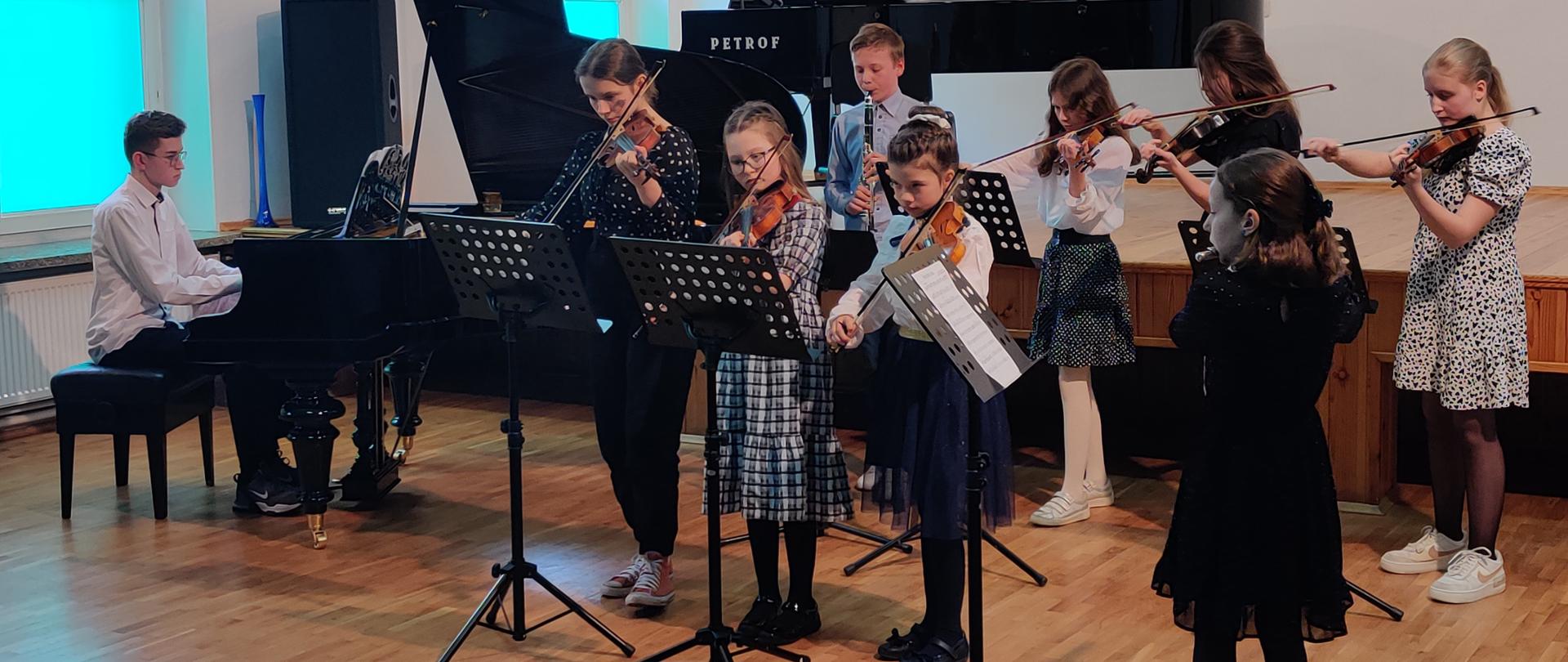 Zdjęcie przedstawiające uczestników szkolnego konkursu podczas gry na instrumentach muzycznych w auli szkoły.