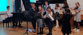 Zdjęcie przedstawiające uczestników szkolnego konkursu podczas gry na instrumentach muzycznych w auli szkoły.
