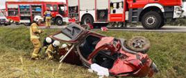 Strażacy wykonują czynności ratownicze przy pojeździe, który brał udział w wypadku komunikacyjnym. Pojazd znajduje się w rowie.