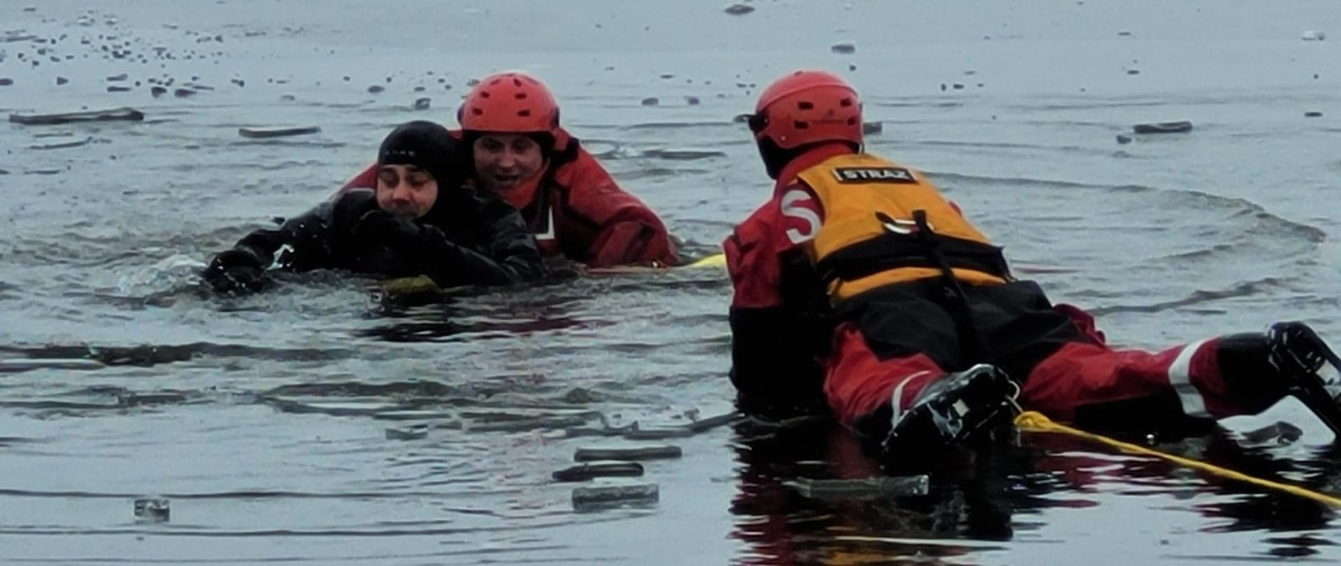 dwóch strażaków w czerwonych ubraniach nie zatapialnych którzy ratują osobę będąca w wodzie.