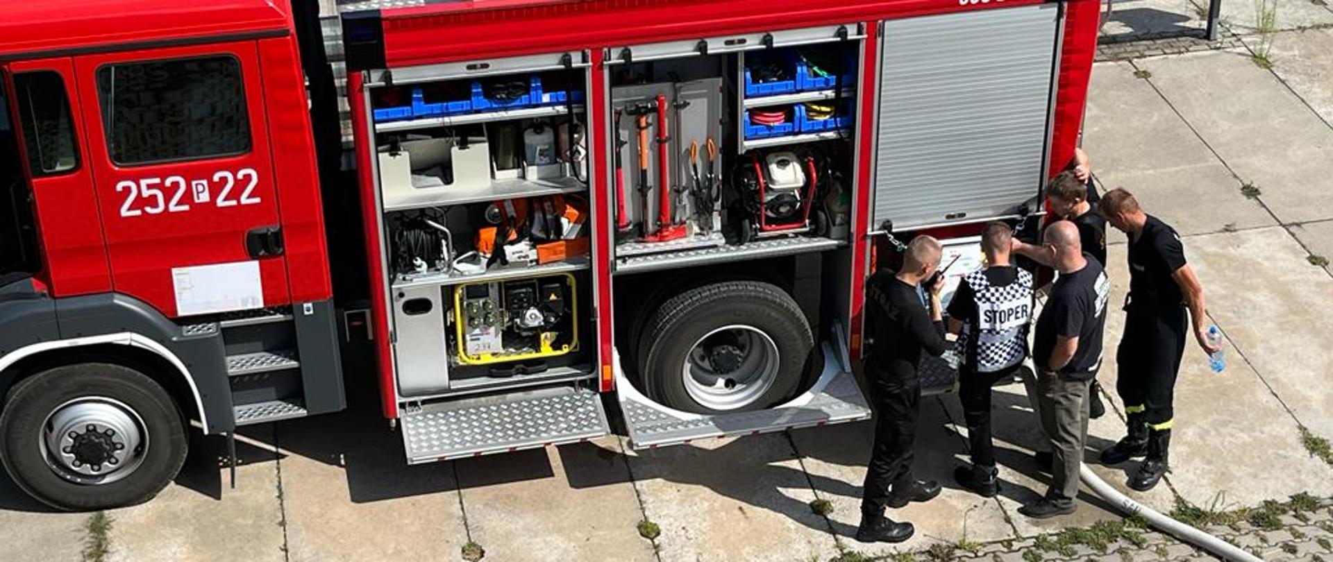 grupa mężczyzn stoi przy strażackim samochodzie