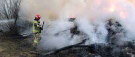 Strażak przegarniający stert tlącego się siana, duże ilości dymu