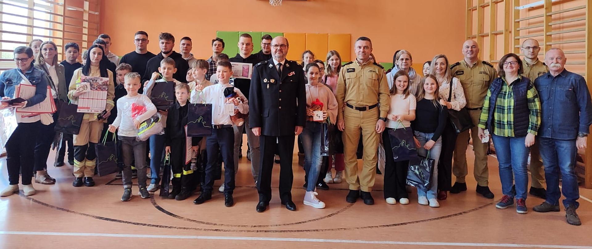 Wszyscy uczestniczy turnieju stoją w pomieszczeniu sali gimnastycznej. Laureaci stoją w pierwszym rzędzie z nagrodami. 