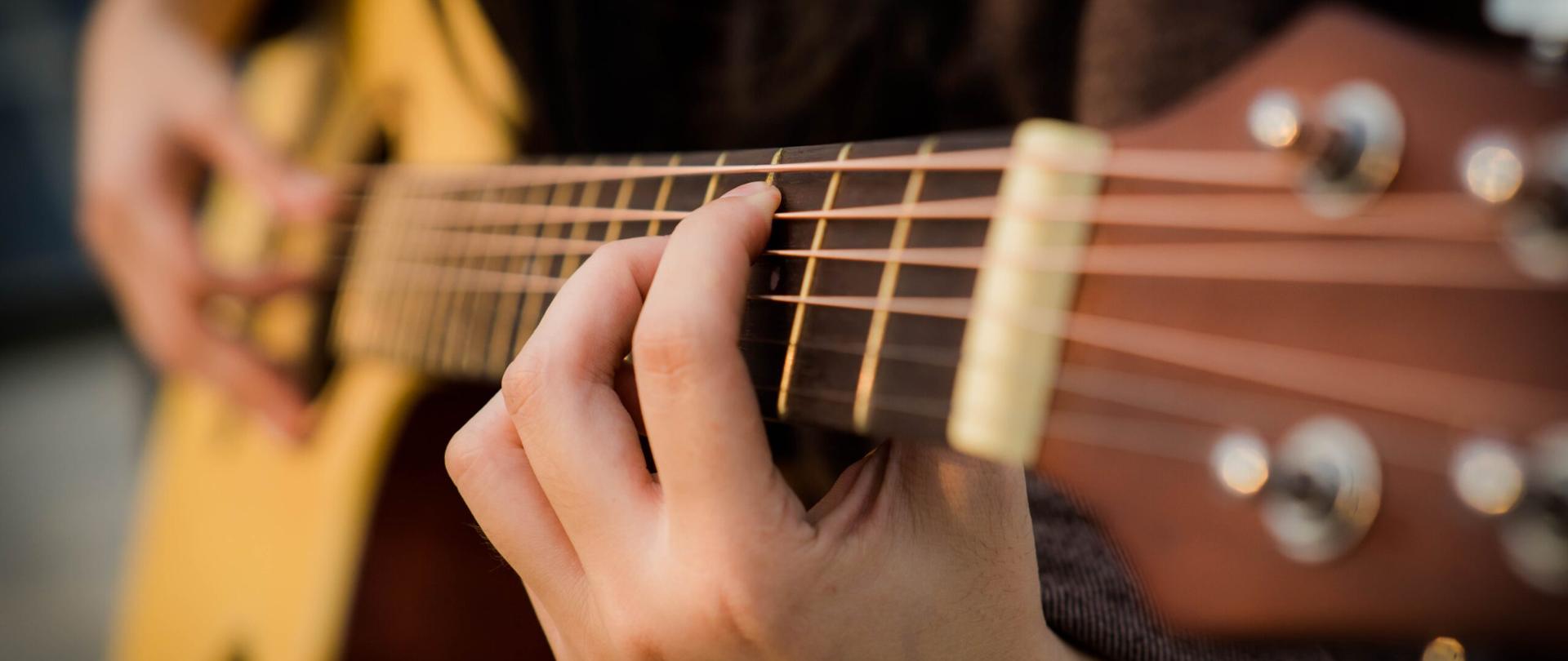 Zdjęcie na którym widać rozmyty fragment gitary oraz dłonie na niej grające