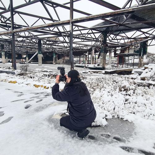 Fotografia przedstawia funkcjonariuszkę Narodowej Policji Ukrainy dokumentującej zniszczenia wojenne za pomocą aparatu fotograficznego w trakcie szkolenia.