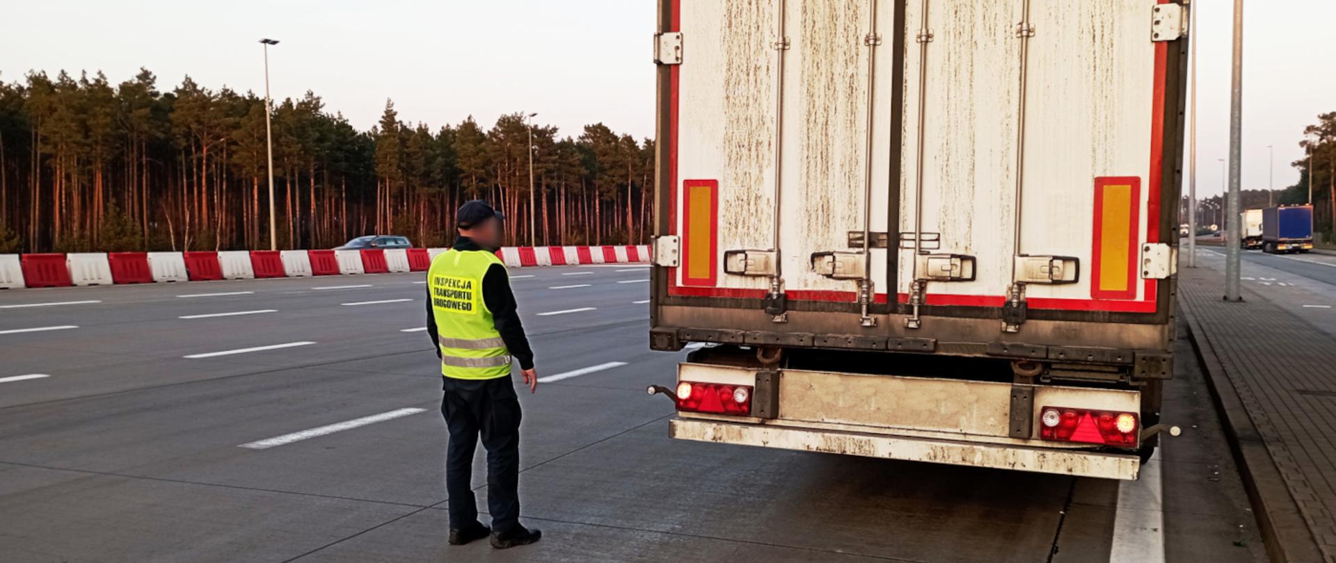 Ciężarówka w trakcie kontroli przeprowadzonej przez inspektorów lubuskiej ITD. Na zdjęciu zatrzymany zespół pojazdów, którego oględzin dokonuje inspektor ITD. W tle ruch samochodowy.