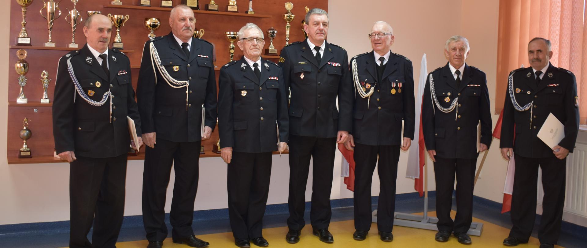 Zdjęcie przedstawia druhów, którzy otrzymali decyzje o przyznaniu świadczenia ratowniczego z komendantem powiatowym Państwowej Straży Pożarnej w Pińczowie bryg. Grzegorzem Karwatem