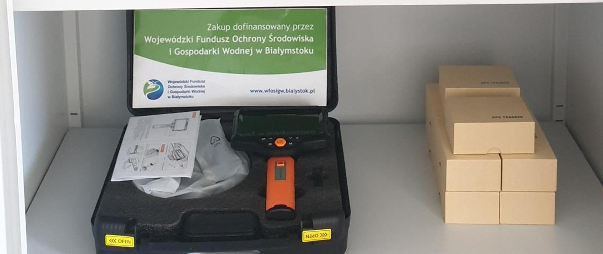 Widoczne przedmioty które są umieszczone na półkach w szafie. Na niektórych rzeczach widnieje logo z Wojewódzkiego Funduszu Ochrony Środowiska i Gospodarki Wodnej w Białymstoku