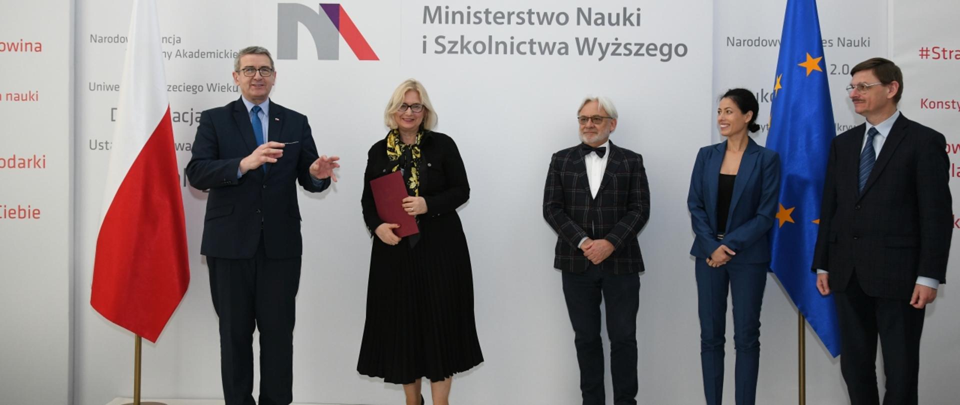 Uczestnicy spotkania stoją na tle ściany z logiem MNiSW.