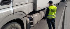 Inspektor ITD stoi obok ciężarówki zatrzymanej do kontroli drogowej i ocenia pojemność zbiorników paliwa.