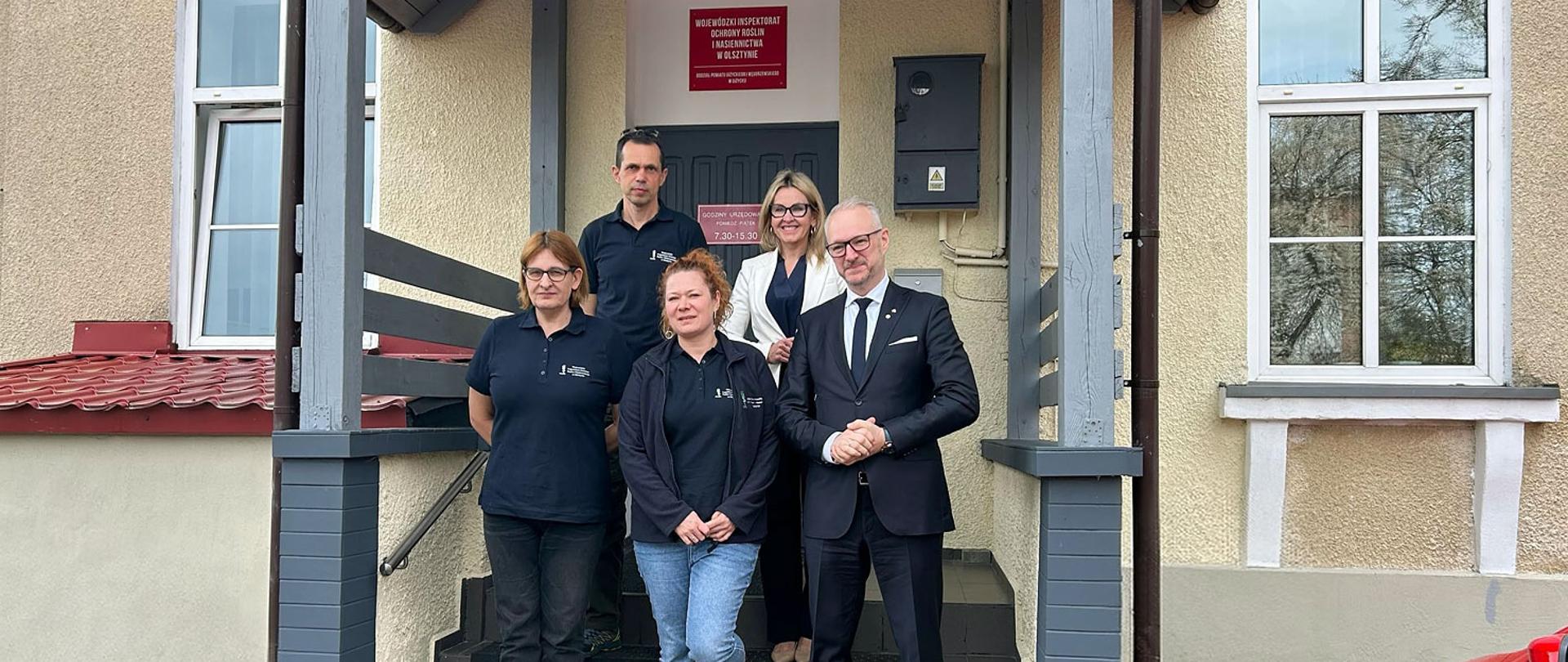 Pięć osób pozuje do zdjęcia grupowego przed wejściem do budynku oddziału WIORiN w Gizycku