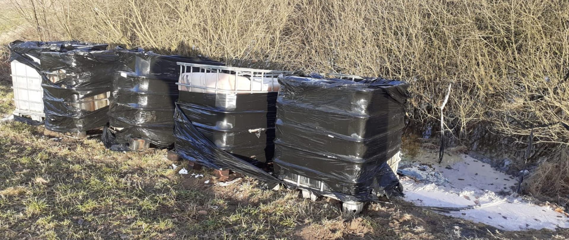 Piec zbiorników DPPL ustawionych w szeregu na polu, częściowo owinięte czarną folią.