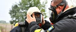 strażacy ubierają się w sprzęt ODO jeden sprawdza poprawność założenia maski oddechowej do aparatu