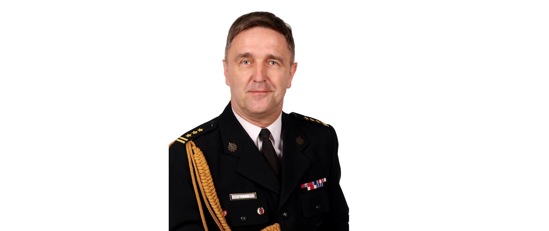Mężczyzna, ciemny blondyn, lekko uśmiechnięty w białej koszuli z krawatem i granatowej marynarce munduru, ze złotymi dystynkcjami.
