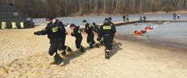 Na zdjęciu widać funkcjonariuszy Państwowej Straży Pożarnej podczas ćwiczeń na zbiorniku wodnym. Funkcjonariusze ćwiczą wyciąganie z wody (lodu) osób poszkodowanych. 