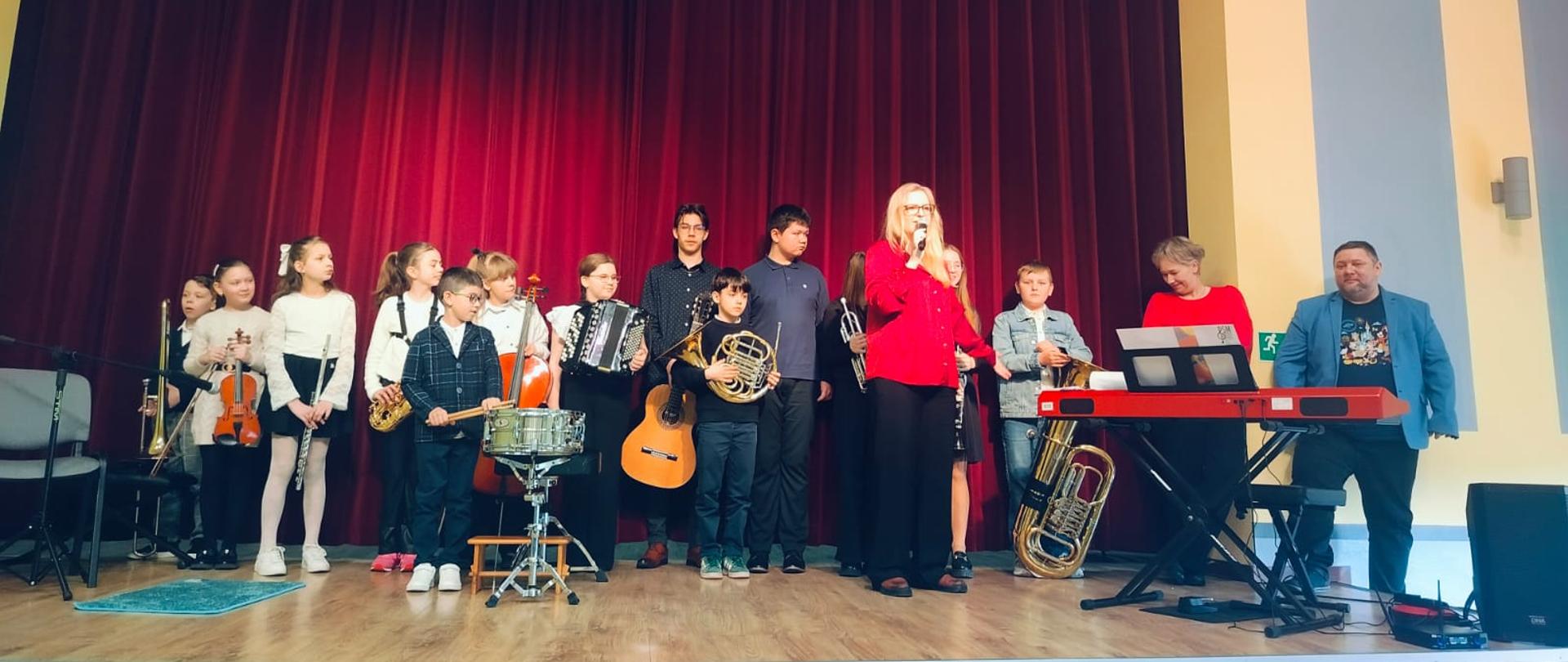 na scenie uczniowie i nauczyciele biorący udział w koncercie
