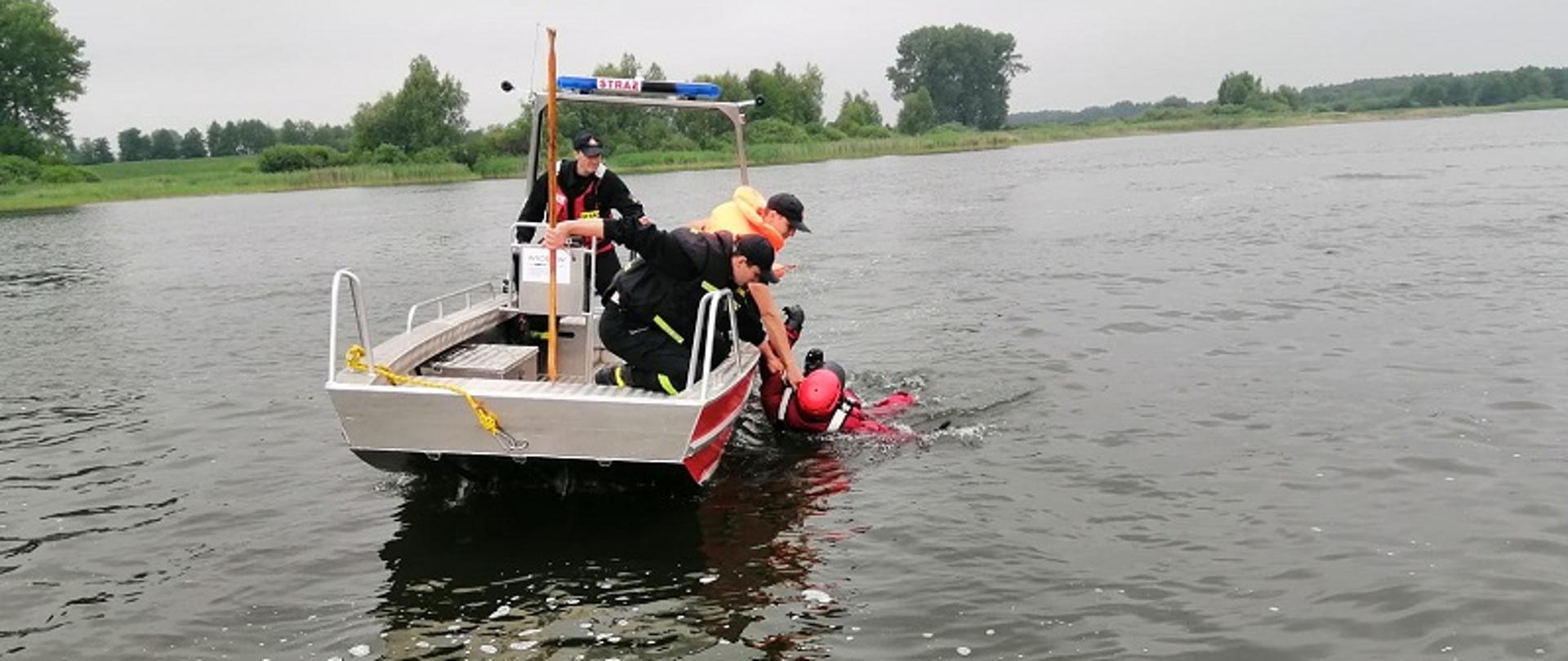 Zdjęcie przedstawia strażaków na łodzi ćwiczących podejmowanie pozoranta z wody na łódź ratowniczą.
