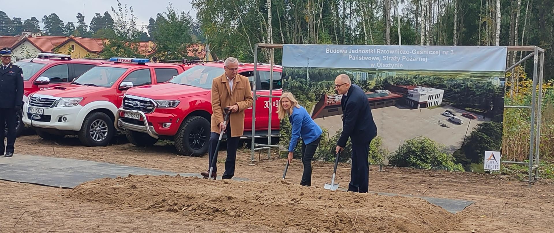 Dwóch mężczyzn i jedna kobieta kopią łopatami 